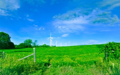 9 white wind turbines set against a blue sky dotted with whispy white and grey cloud. Lush green fields fill the foregournd, and are surrounded by green leafy treelines and some wood and wire fences. Real Estate & Homes for sale - Communites Home Page